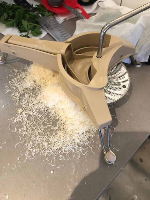 Parmesan Cheese and Grater Medium. an wider view of a block wedge of  parmesan cheese with shredded pieces all around and a metal cheese grater  on a cutting board Stock Photo