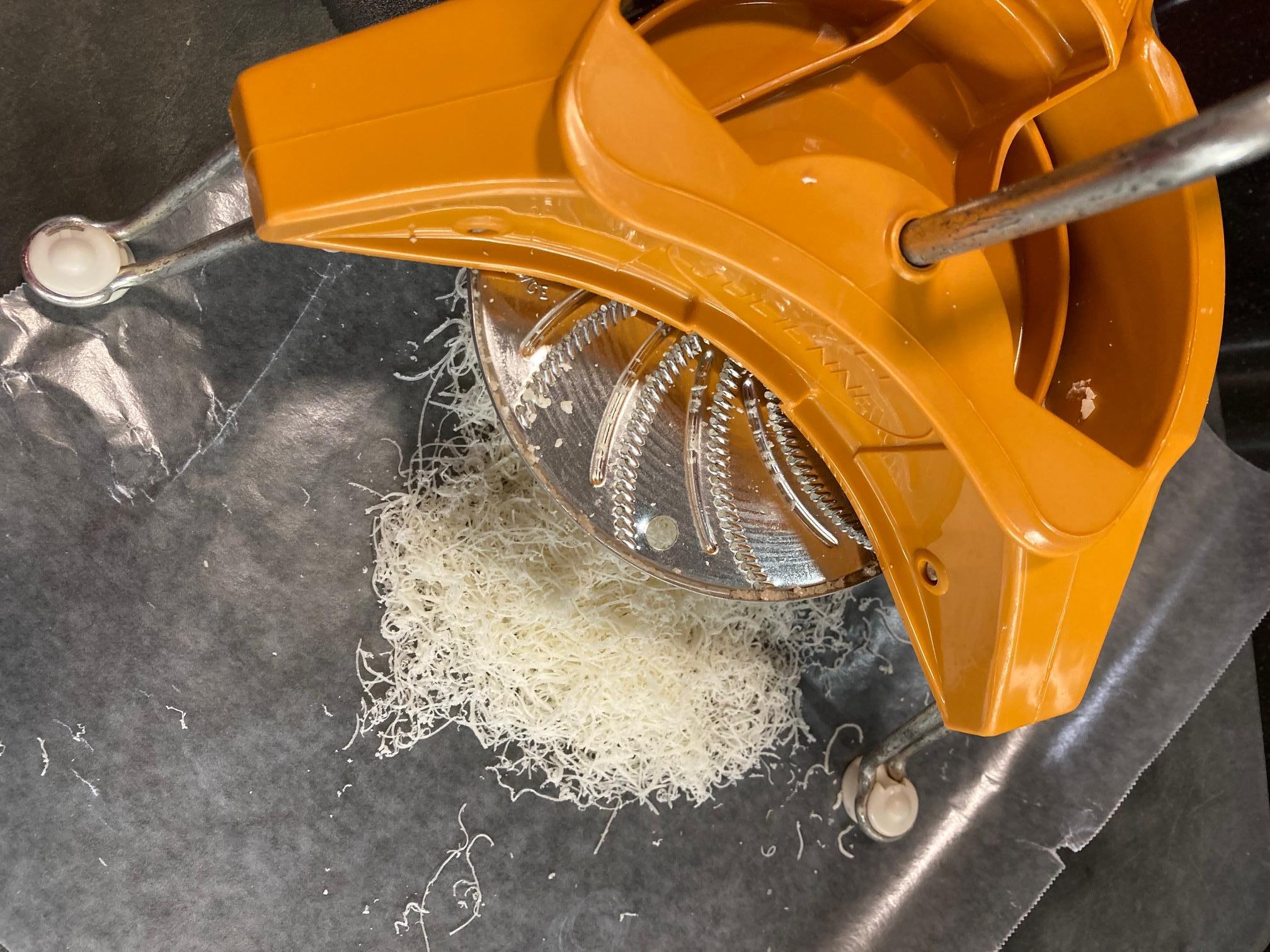 Parmesan Cheese and Grater Medium. an wider view of a block wedge of  parmesan cheese with shredded pieces all around and a metal cheese grater  on a cutting board Stock Photo